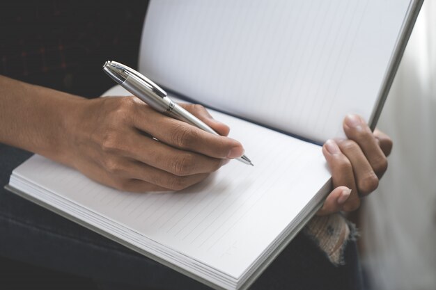 El diseñador creativo casual femenino está escribiendo la nota en el cuaderno