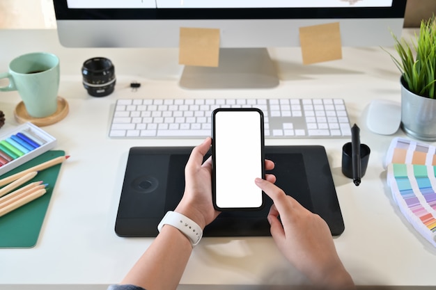 Diseñador creativo que sostiene y usa el teléfono móvil inteligente en el lugar de trabajo del estudio