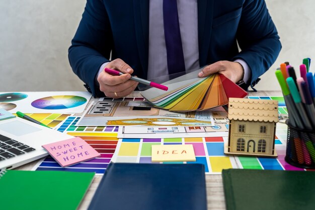 El diseñador desarrolla un boceto de la ilustración interior con una combinación de colores del material en una mesa, lugar de trabajo de oficina. Escritorio de un arquitecto e interiorista con muestras de equipos y materiales