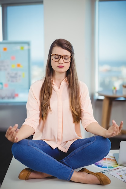 Diseñador gráfico femenino sentado en la mesa y meditando