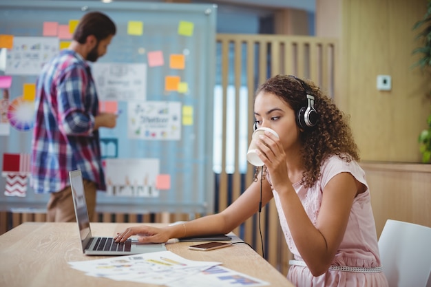 Foto diseñador gráfico femenino tomando café mientras usa la computadora portátil