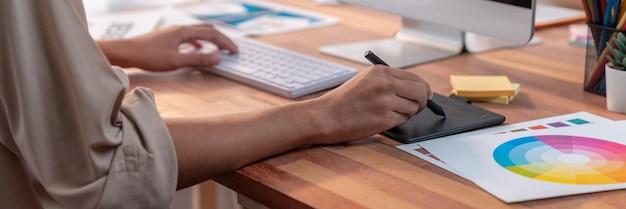 El diseñador gráfico trabaja en una computadora portátil y con un bolígrafo de dibujo gráfico mientras hace una lluvia de ideas de diseño único con un equipo gráfico profesional en un lugar de trabajo de estudio digital moderno.