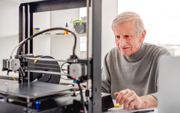 Diseñador de hombre adulto mirando la impresora 3D durante el proceso de desarrollo del trabajo
