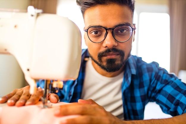 Diseñador de hombre árabe cosiendo ropa en máquina de coser en casa de trabajo de estudio