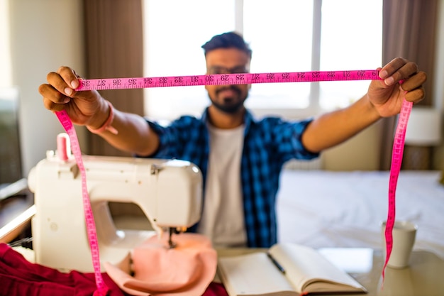 Diseñador de hombre árabe cosiendo ropa en máquina de coser en casa de trabajo de estudio