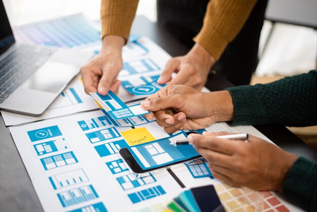 El diseñador de la interfaz de usuario y el diseñador del equipo de desarrolladores de la experiencia de usuario hacen una lluvia de ideas sobre el diseño de estructura alámbrica de la interfaz de la aplicación móvil con el código de color y el resumen del cliente en la oficina modernaxA