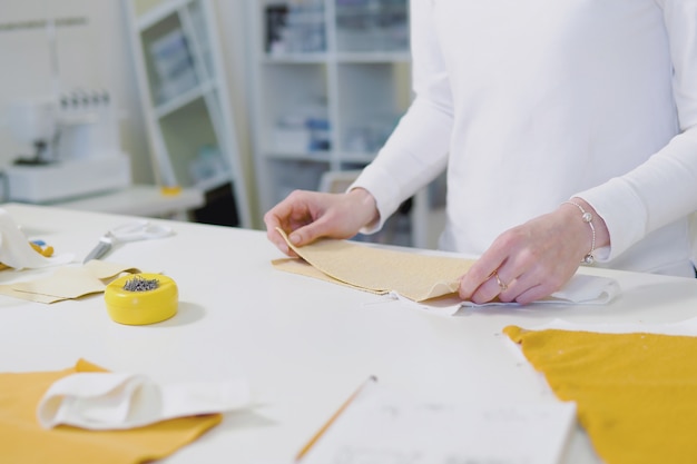Diseñador de moda o sastrería cortando tela mientras trabaja con bocetos de dibujo y material en la mesa de trabajo