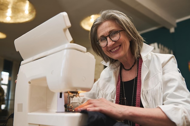 Diseñador de moda sastre modista de alcantarillado en fábrica o taller de diseño de ropa Mujer madura costurera en máquina de coser