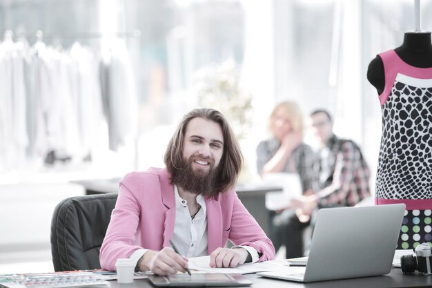 Diseñador de moda sonriente en la mesa en un estudio moderno