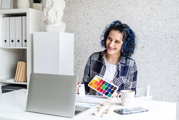 Foto diseñador que trabaja con paletas de colores y portátil en su estudio de arte