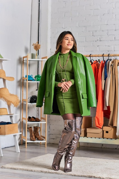 diseñador de ropa asiático creativo posando con chaqueta de cuero verde en su atelier personal pequeño negocio