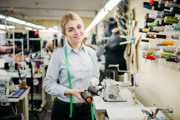 Diseñador de ropa con hilos de colores en las manos, fabricado en fábrica de costura. Costurera femenina en tela de vestir, confección o sastrería