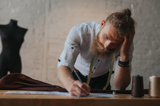 diseñador de ropa joven moderno en el proceso de trabajo, diseñador de ropa con pelo largo y barba