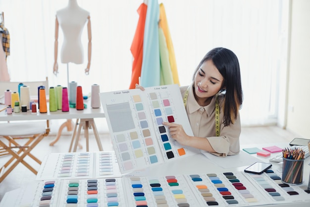 La diseñadora asiática está pensando y diseñando ropa para que los clientes pidan artículos en el escritorio del diseñador en el estudio. Los diseñadores de ropa están trabajando en la oficina. Concepto de diseñador de inicio.