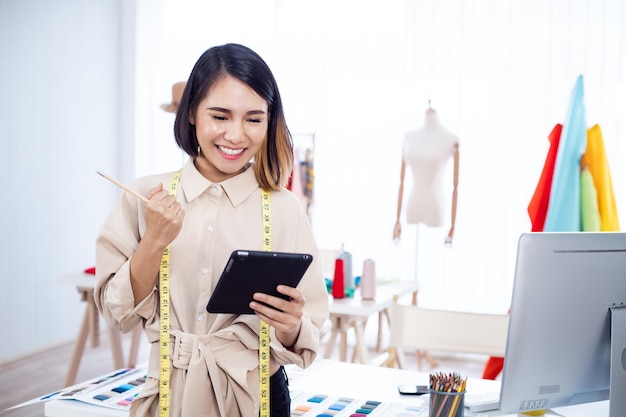 Diseñadora asiática pensando en diseñar ropa en una tableta en el estudio.