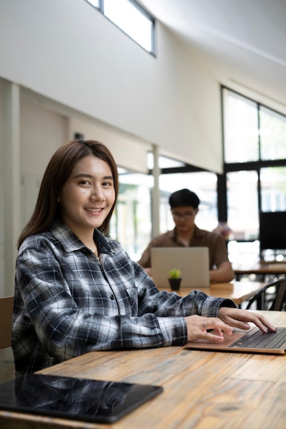 Foto diseñadora asiática sentada en una oficina creativa con su colega y sonriendo a la cámara