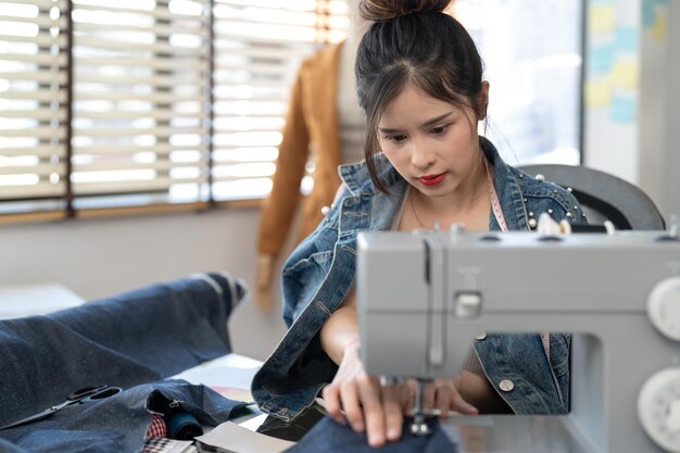 Foto diseñadora asiática usando máquina de coser confeccionando nuevas colecciones de ropa en el taller de costura