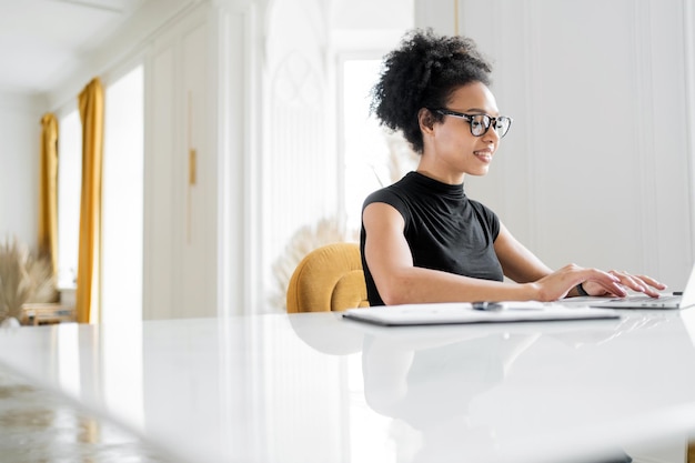 La diseñadora es una mujer con anteojos que trabaja en línea en la oficina usando una computadora de tableta coworking