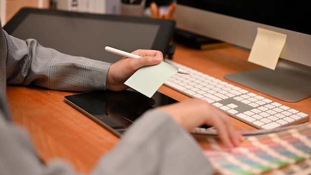 La diseñadora gráfica que trabaja en el escritorio de su oficina se sienta frente a la computadora recortada