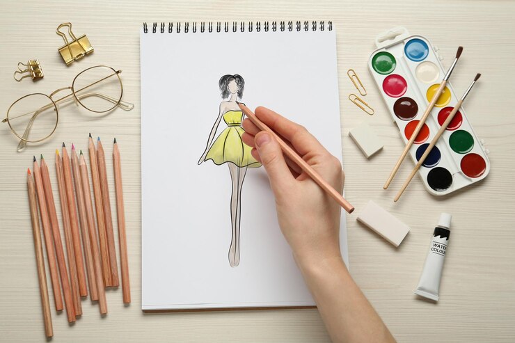 Foto diseñadora de moda creando una nueva apariencia mujer dibujando bocetos en bloc con lápiz en la vista superior de la mesa de madera blanca