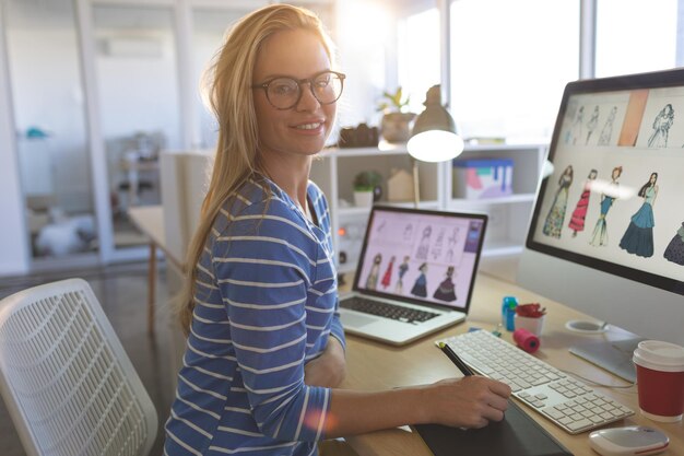Diseñadora de moda mirando a la cámara mientras trabaja en el escritorio
