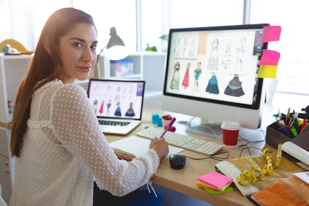 Diseñadora de moda mirando a la cámara mientras trabaja en el escritorio