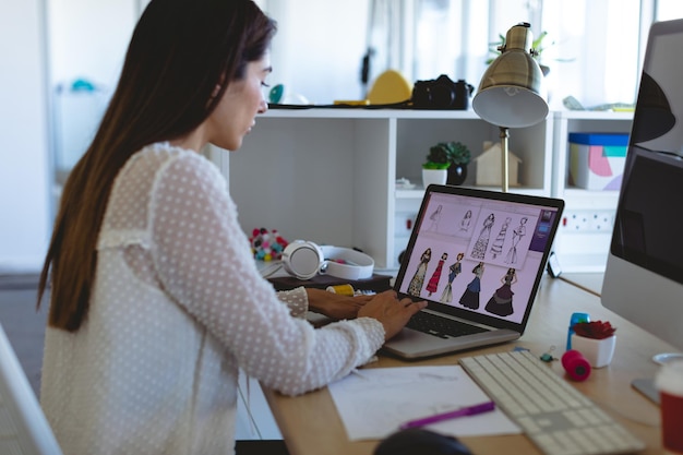 Diseñadora de moda que trabaja en una computadora portátil en un escritorio en una oficina moderna
