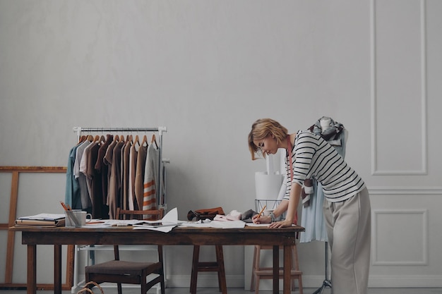 Diseñadora de moda segura haciendo bocetos mientras está de pie cerca de su lugar de trabajo