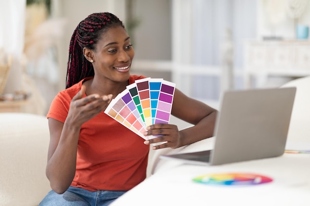 Diseñadora negra sonriente que usa una computadora portátil para una videollamada con el cliente