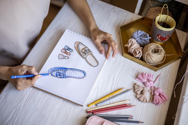 Diseñadora de ropa y zapatos de mujer creativa dibujando bocetos coloreados de zapatillas trabajando en el escritorio de casa