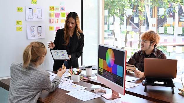 Diseñadora de sitios web que muestra el diseño de la interfaz de usuario en una tableta digital al equipo creativo en la presentación de la oficina