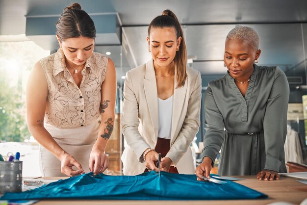 Los diseñadores son como magos de la moda. Foto de un grupo de jóvenes diseñadoras cortando material en una boutique.