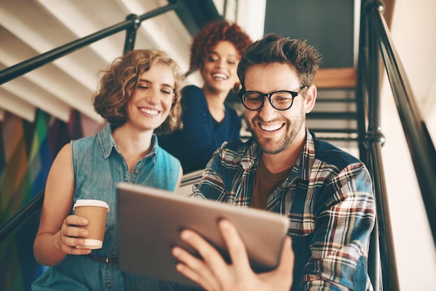 Diseñadores de trabajo en equipo o gente feliz con tableta o informe en línea en una reunión para analizar los pasos Sonrisa de Internet o grupo de empleados creativos en una oficina moderna de inicio en las escaleras para una noticia digital