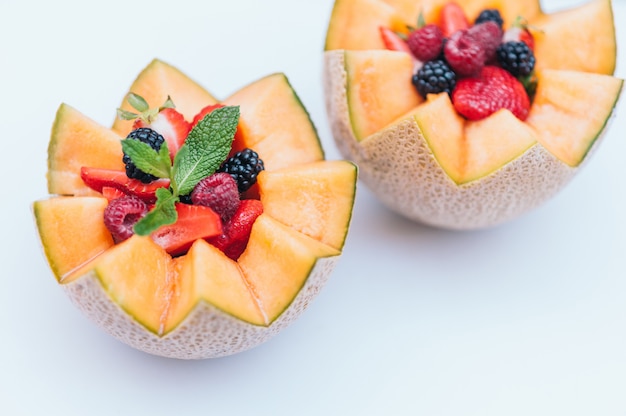 Diseño de alimentos y concepto de nutrición saludable. Deliciosa frambuesa fresca, fresa y mora con menta en melón tallado. Cantalupo con fruta sobre fondo blanco.