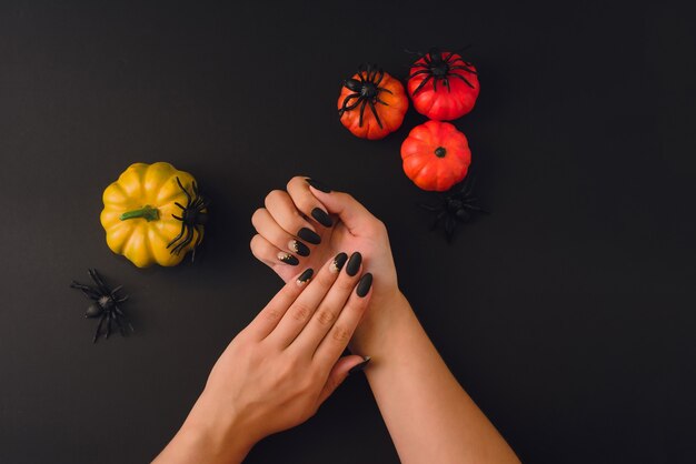 Diseño de arte de uñas de Halloween. Lay Flat con calabazas, arañas y hermosa manicura en manos sobre fondo negro