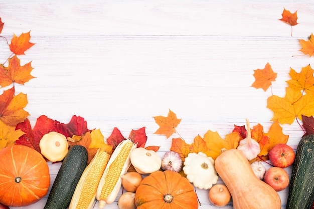 Diseño con calabaza, maíz, otras verduras y hojas de otoño. Vista superior sobre un fondo de madera clara.