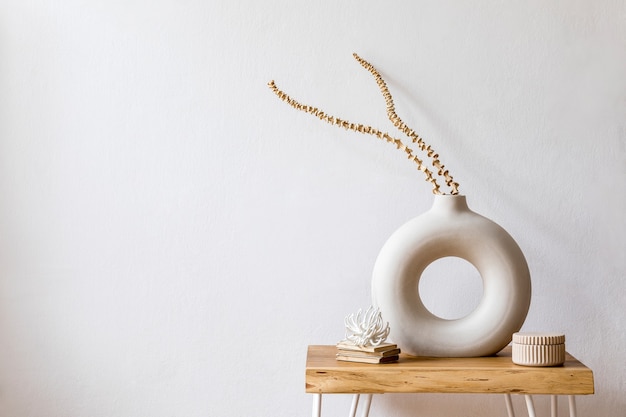 Diseño de composición de flores secas en elegante florero, libros y mesa de centro de madera en el interior blanco de la sala de estar Copie el espacio. Pared blanca.