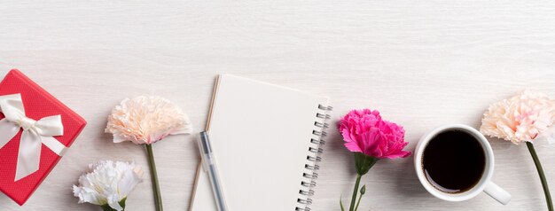 Diseño concpet del saludo del día de la madre con flor de clavel, idea de regalo de vacaciones y diario de cuaderno en el fondo del escritorio de la madre.