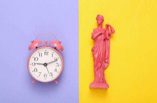 Diseño creativo Estatua de la diosa griega antigua rosa con reloj despertador sobre fondo amarillo púrpura Plano Vista superior