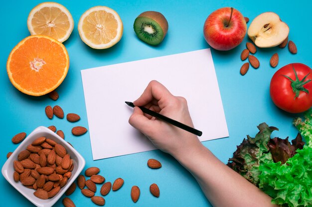 Foto diseño creativo hecho de varias frutas, verduras y nueces con hoja de papel blanco espacio libre