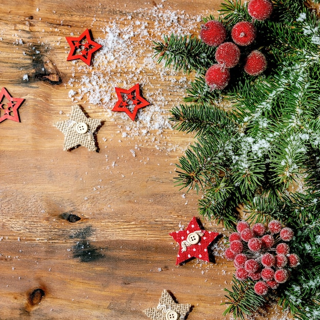 Diseño creativo de Navidad año nuevo o tarjeta de felicitación con ramas de abeto, frutos rojos y estrellas sobre fondo de madera. Endecha plana, espacio de copia, imagen cuadrada