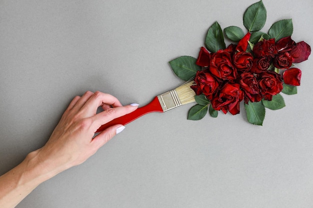 Diseño creativo con pincel y flores rosas rojas sobre fondo gris Cepillo de mano de mujer