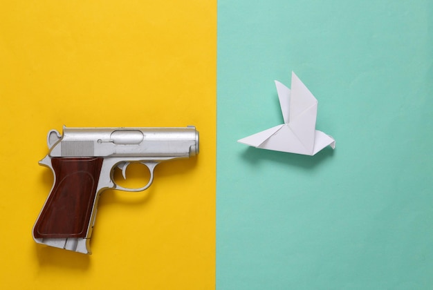 Diseño creativo de pistola y paloma de origami sobre fondo azul amarillo PeaceNo war Vista superior