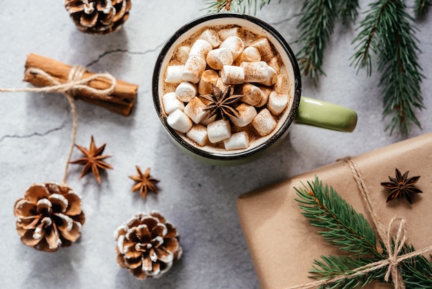 Diseño creativo de vacaciones navideñas con taza púrpura de malvavisco, chocolate caliente, pino y piñas