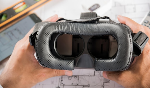 El diseño de edificios arquitectónicos retiene las gafas 3D VR y los planes de construcción con planos de proyectos en papel