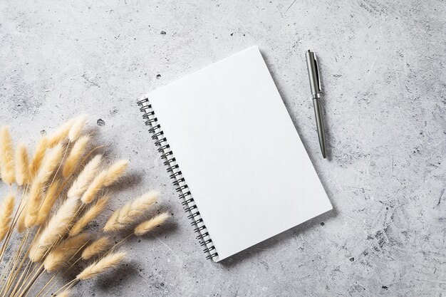 Diseño del espacio de trabajo de la oficina en casa con un bolígrafo blanco vacío y un ramo seco sobre fondo de hormigón gris Vista superior y espacio de copia