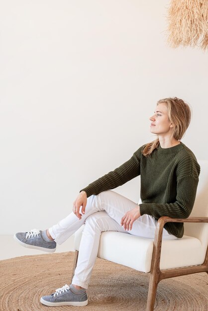 Foto diseño interior minimalista, ligero y aireado. mujer joven atractiva con vaqueros blancos y suéter verde.