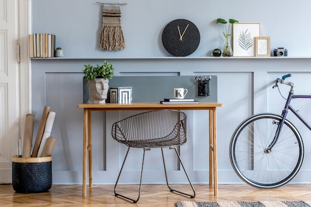 Diseño de interiores escandinavo de oficina en casa con escritorio de madera, silla moderna, paneles de madera con estante, planta, alfombra, bicicleta, material de oficina, taburetes de mármol y elegantes accesorios personales.