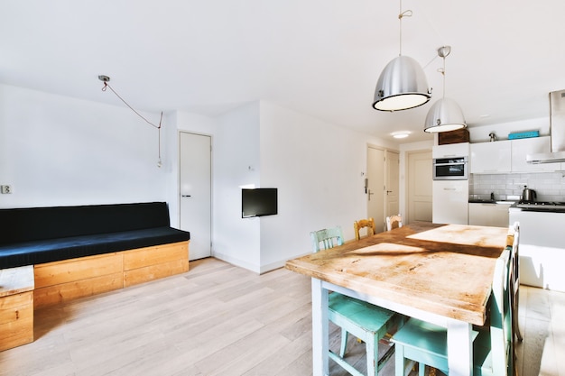 Diseño de interiores de estilo minimalista contemporáneo de un estudio ligero con mesa y sillas de madera en la zona de comedor entre la cocina abierta y la sala de estar con paredes blancas y piso de parquet