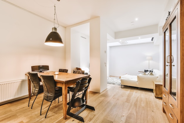 Diseño de interiores de estilo minimalista moderno de apartamento tipo estudio con cocina blanca abierta y zona de comedor con mesa y sillas iluminadas por lámpara de estilo loft